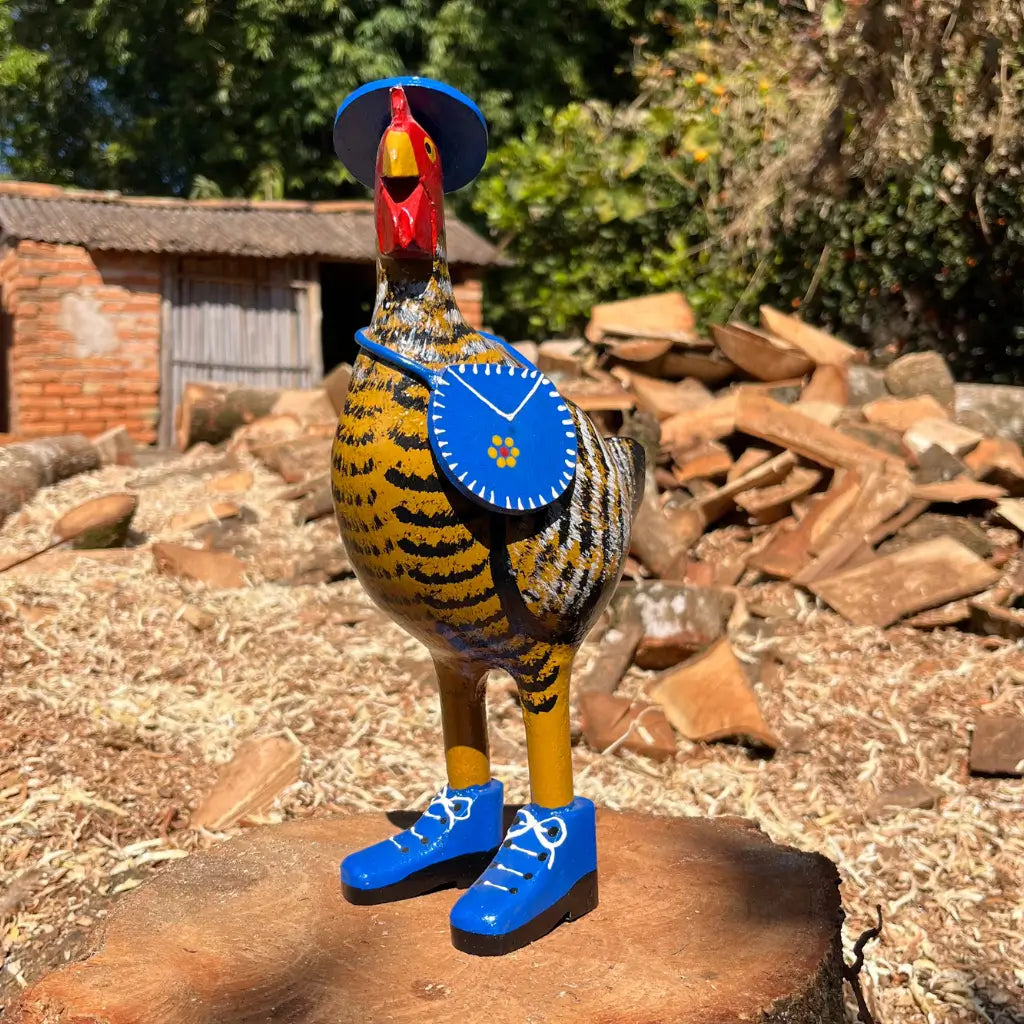 "Uma escultura de madeira de uma galinha caipira de madeira amarela com bota chapeu e bolsa"