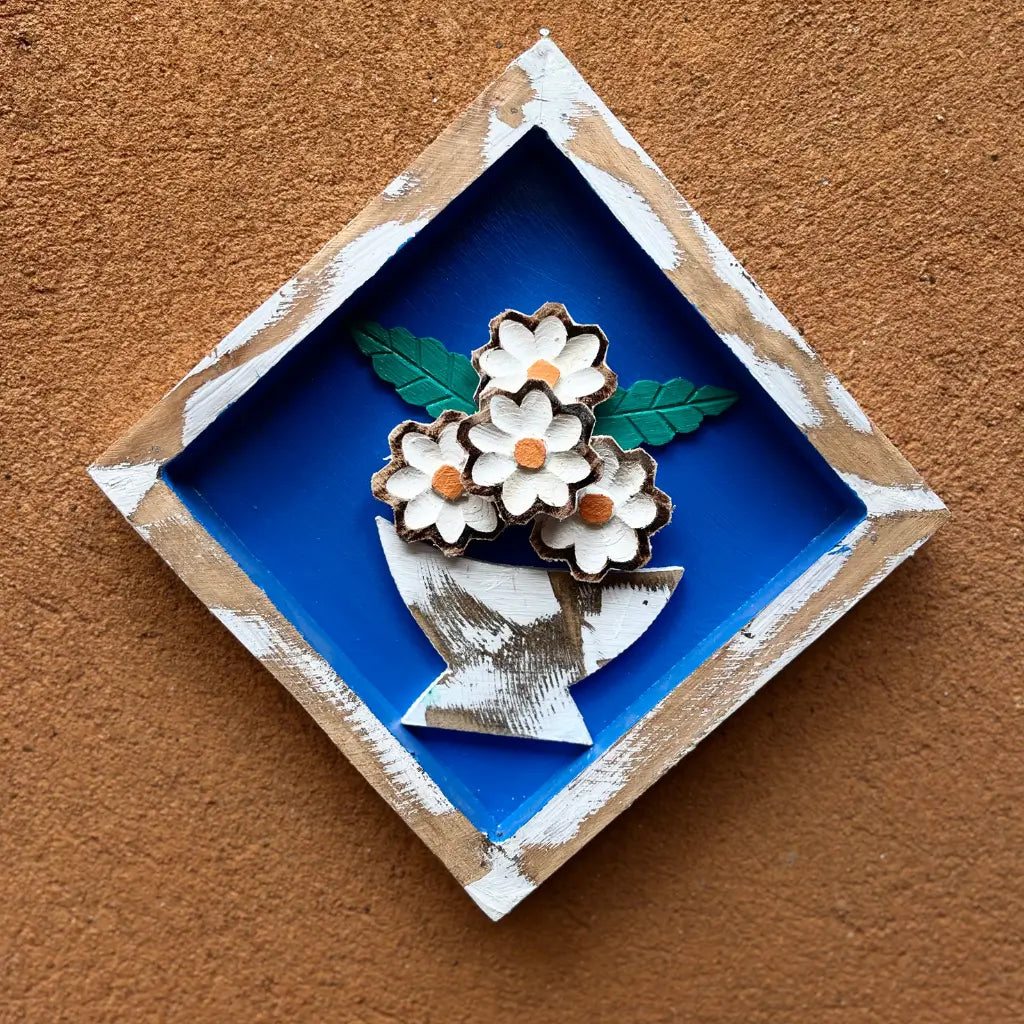 "Um quadro de parede losango em madeira com vaso de flores no fundo azul"