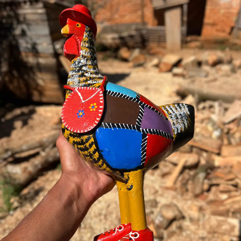 "Uma escultura de galinha caipira amarela com chapeu bolsa e bota com pintura em patchwork"