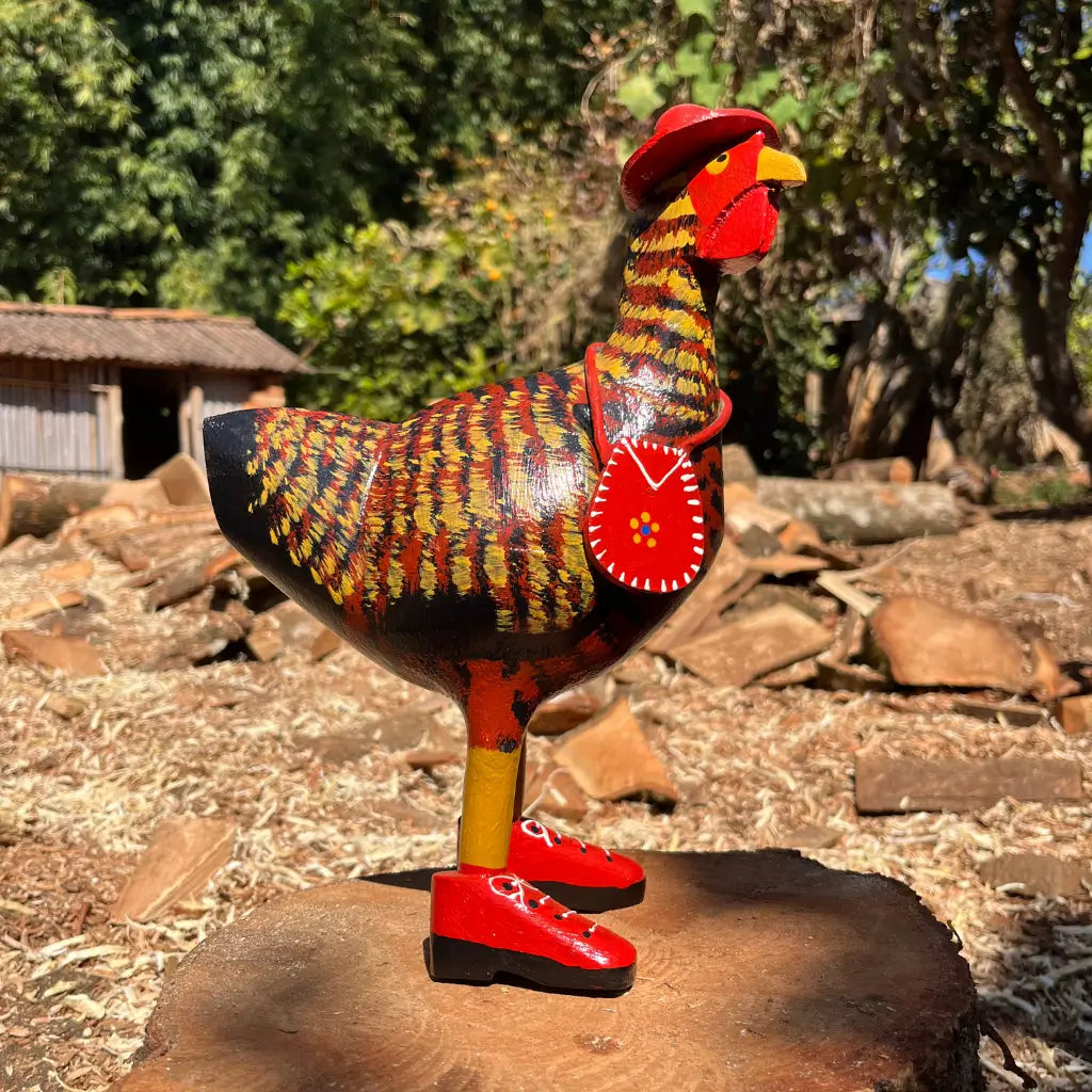 "Uma escultura de madeira de uma galinha caipira de madeira vermelha com bota chapeu e bolsa"
