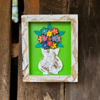 "Um quadro de parede feito de madeira com vaso de flores"