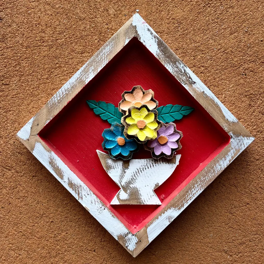 "Um quadro de parede losango em madeira com vaso de flores no fundo vermelho"