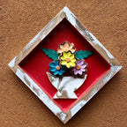 "Um quadro de parede losango em madeira com vaso de flores no fundo vermelho"